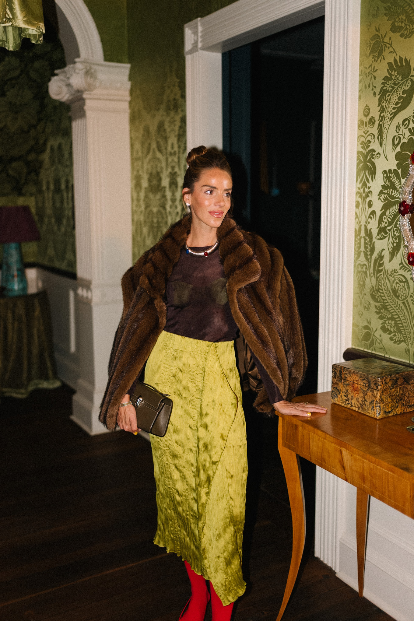 manteau en fausse fourrure marron, haut transparent marron, jupe en soie verte, collants rouges, talons rouges