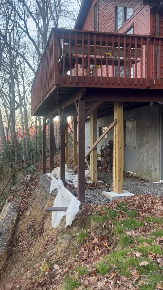 A red house sits a few feet away from where landslides created a 150-foot cliff. Since Helene, the back porch has been reinforced by support beams.