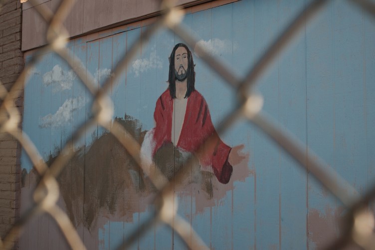A painting of Jesus on a blue wall, behind a chain-link fence. 