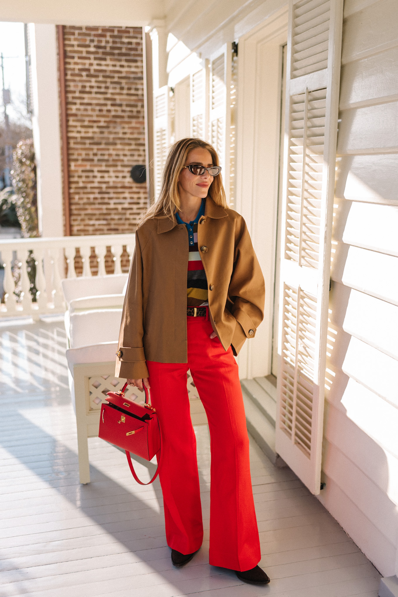 trench court marron, chemise à col rayé, pantalon rouge, sac à main en cuir rouge