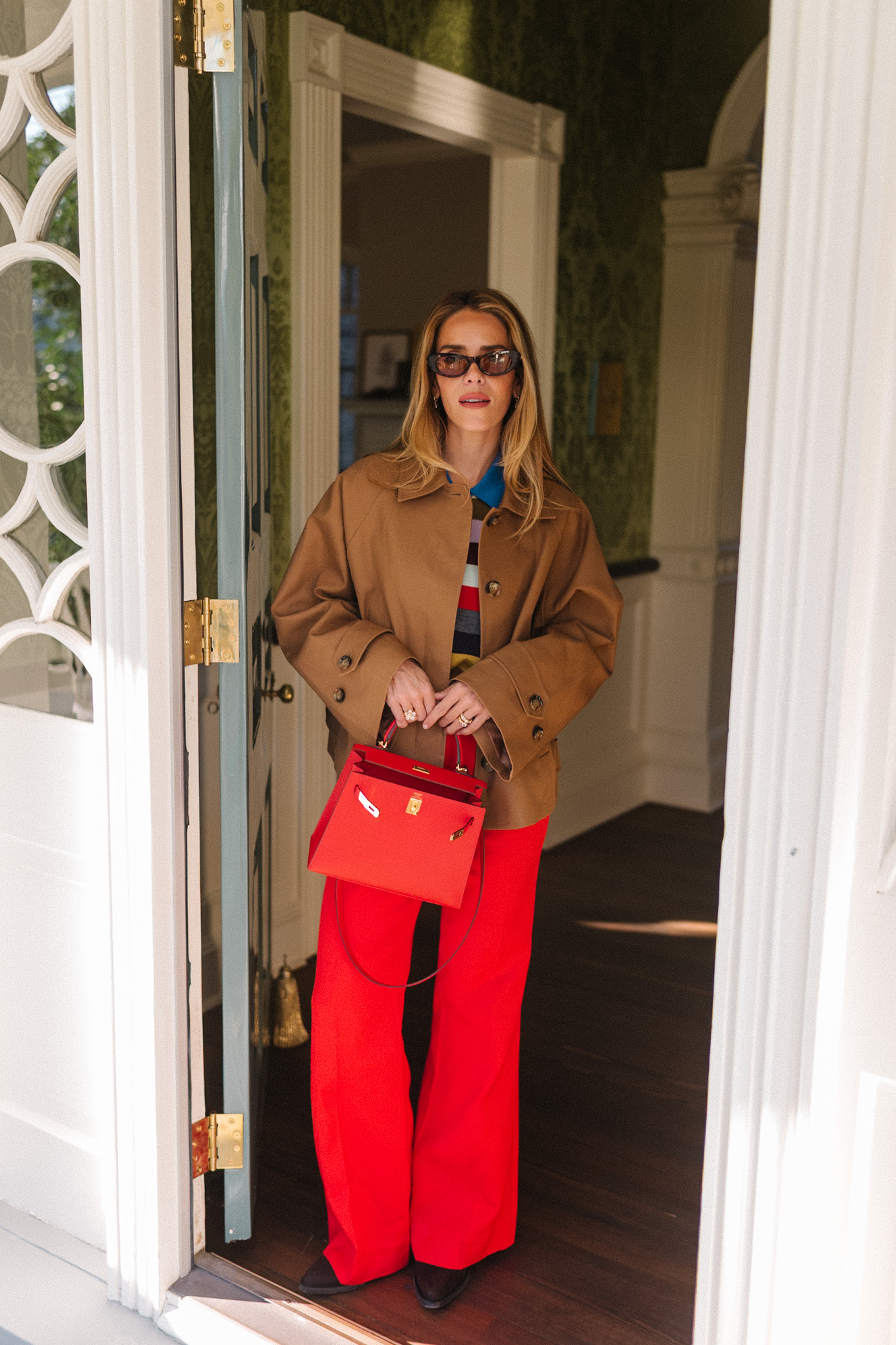 trench court marron, chemise à col rayé, pantalon rouge, sac à main en cuir rouge