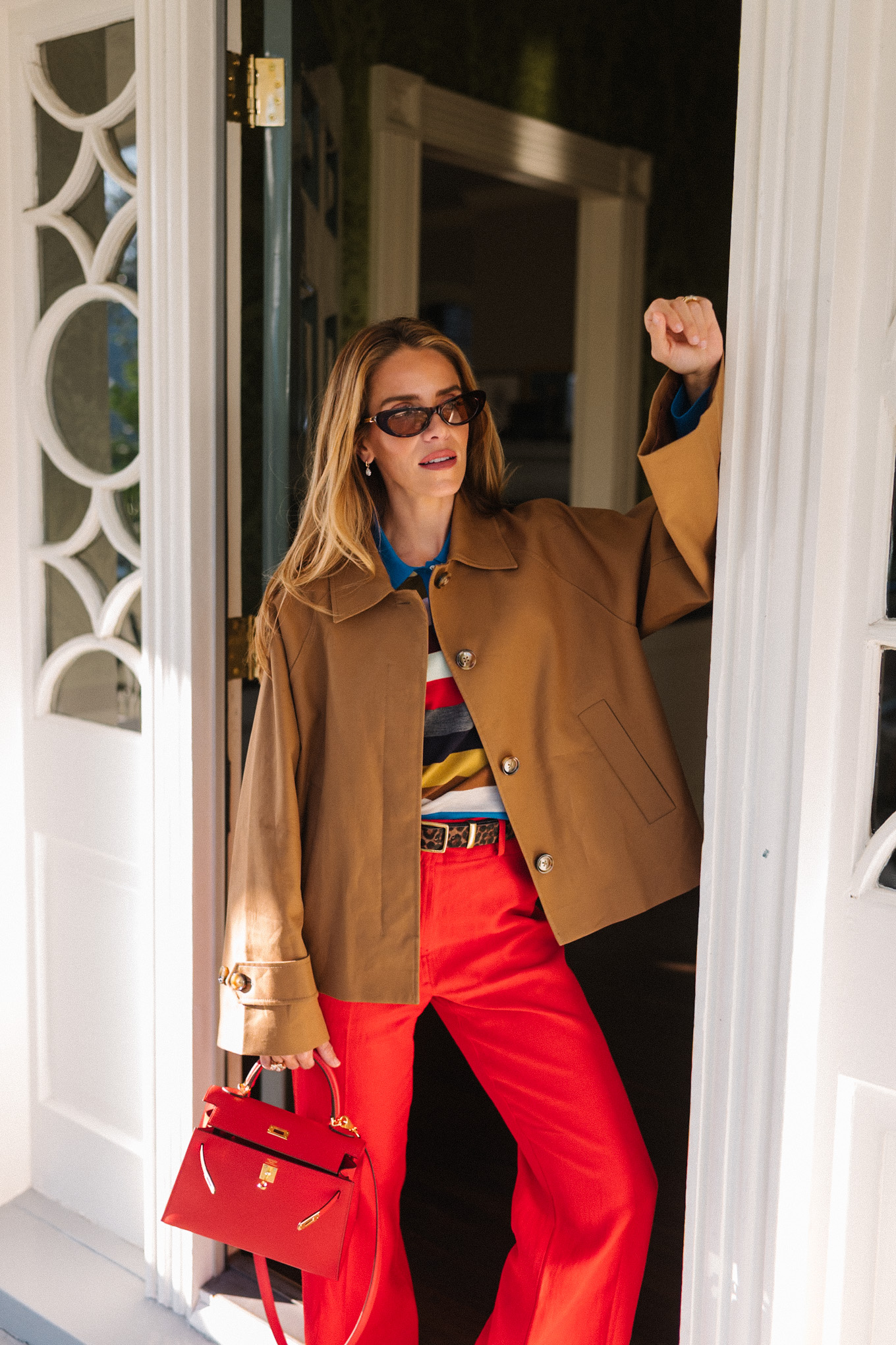 trench court marron, chemise à col rayé, pantalon rouge, sac à main en cuir rouge