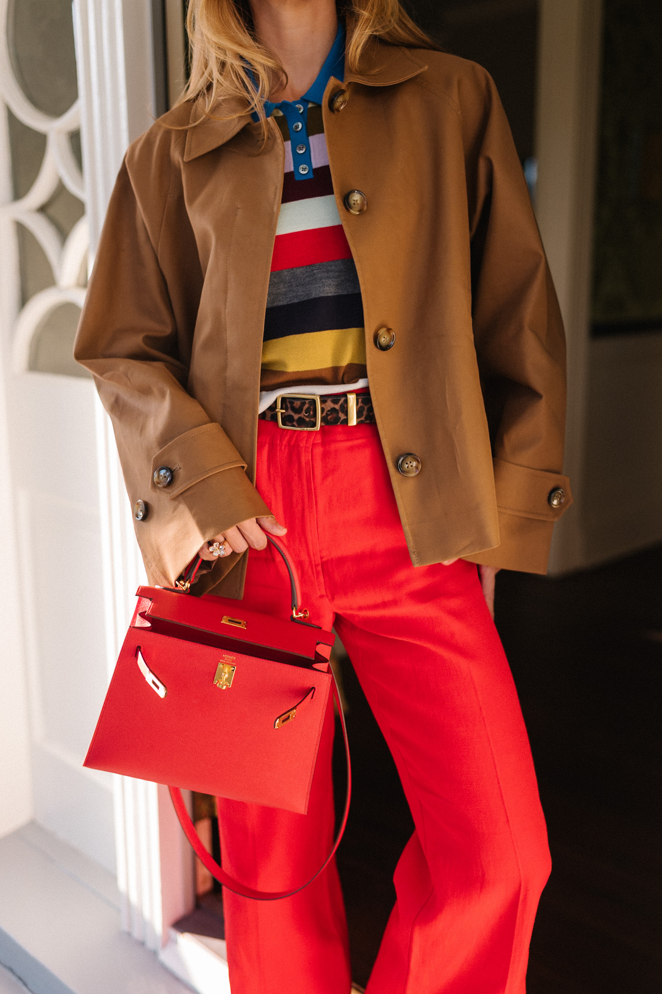 trench court marron, chemise à col rayé, pantalon rouge, sac à main en cuir rouge