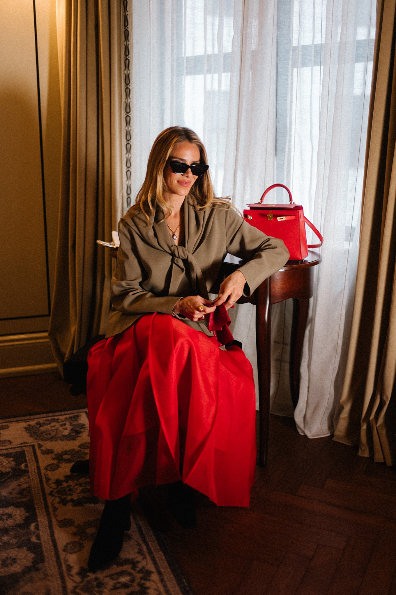 Manteau en peau lainée, écharpe marron clair, blazer, jupe longue rouge, sac à main en cuir rouge