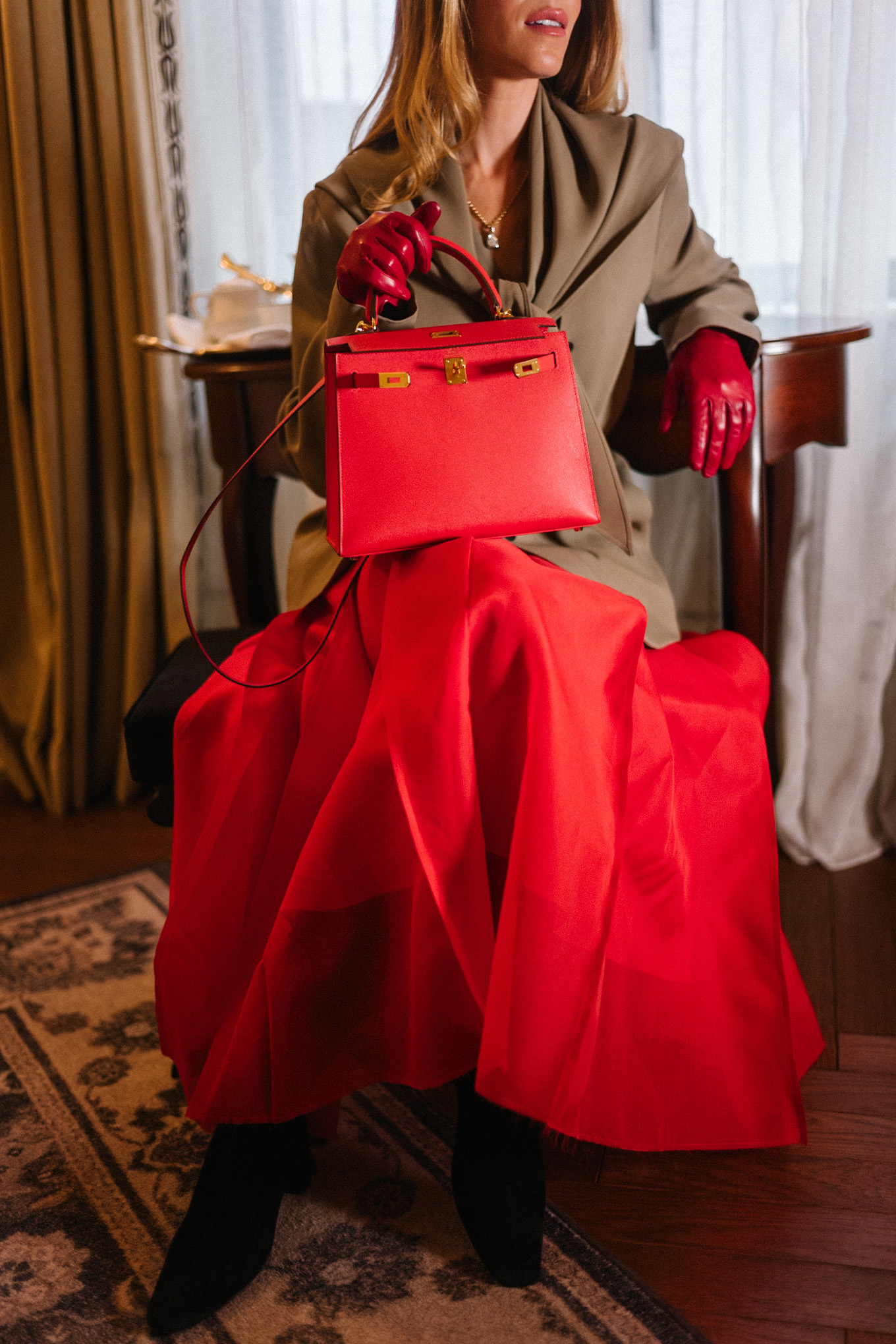 Manteau en peau lainée, écharpe marron clair, blazer, jupe longue rouge, sac à main en cuir rouge