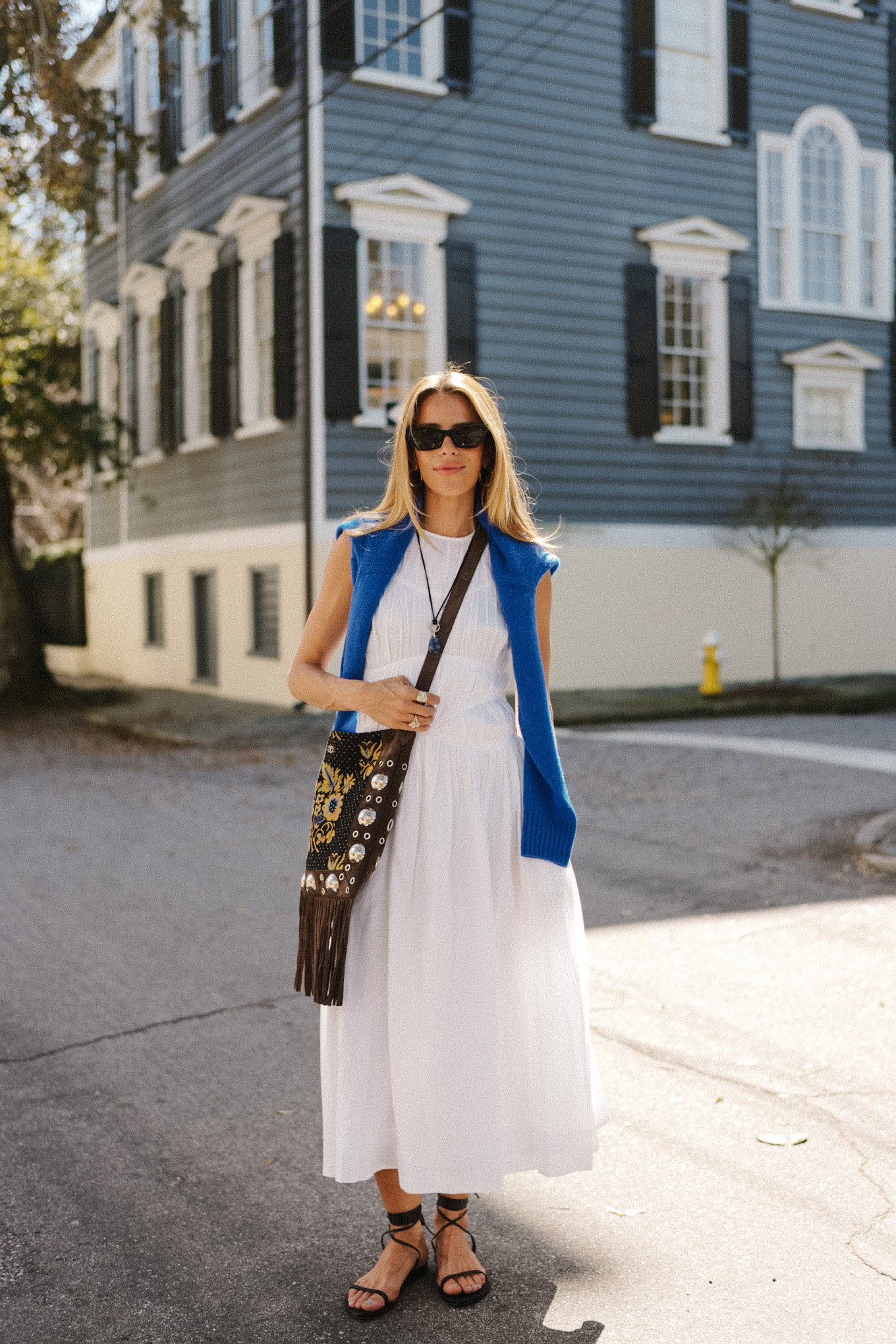 Robe longue blanche, pull bleu, sac en daim à franges