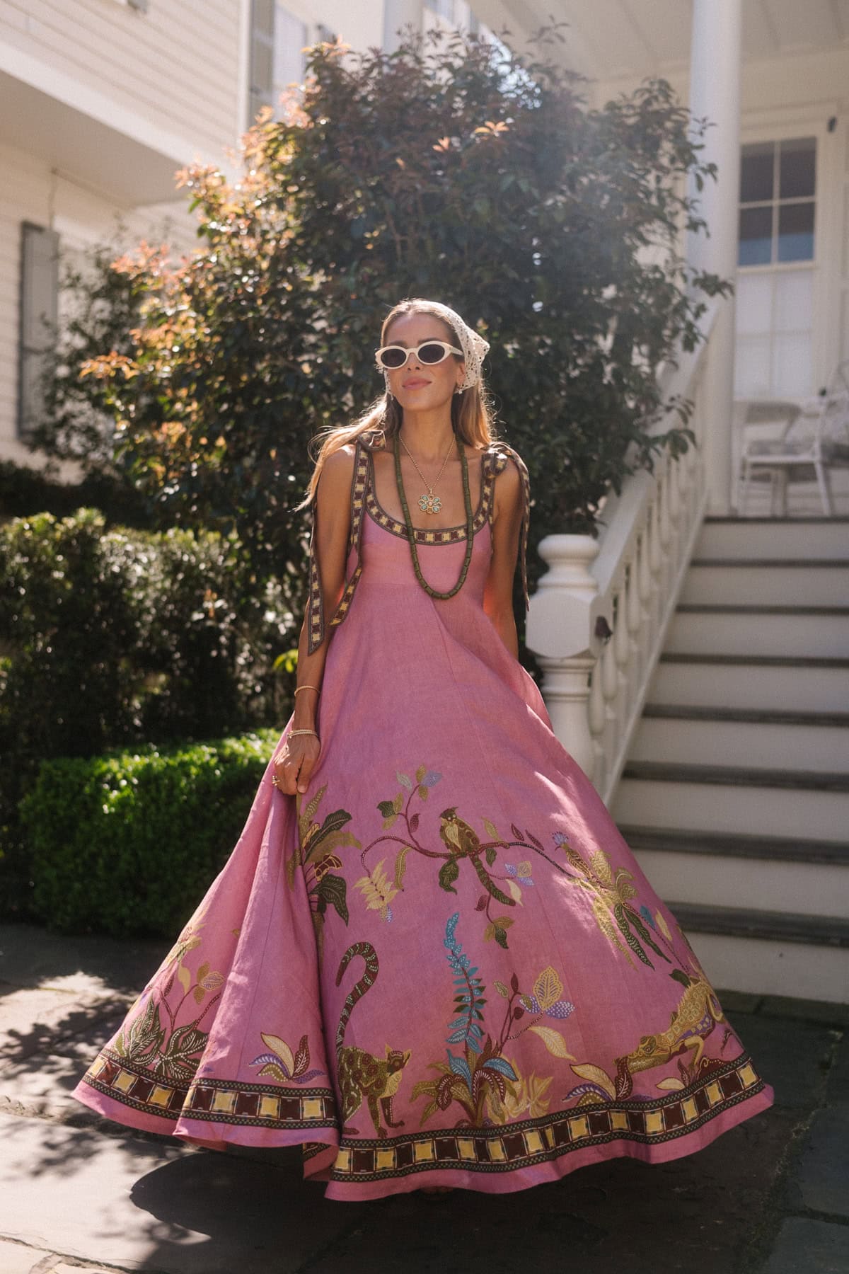 Belle femme en vêtements boho brodés roses avec lunettes de soleil et bijoux.