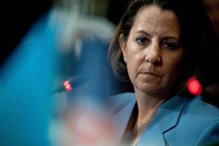 A woman with chin-length brown hair in a blue blazer looks toward the camera. Abstract blue and red light patterns blur in the foreground and background.