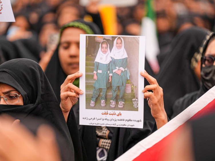 A person in a crowd holds up an image of two young girls posing together, smiling and dressed in green uniforms.