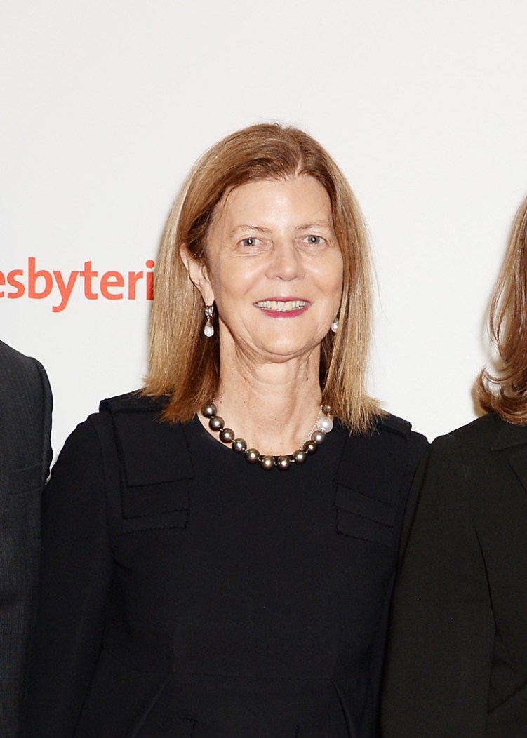 Une femme aux cheveux brun-blond jusqu'aux épaules porte des boucles d'oreilles, un collier et des tenues de soirée noires. 