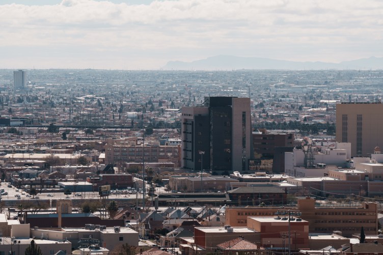A wide landscape of a cluster of tall buildings in downtown El Paso with Ciudad Juarez stretching off in the distance.