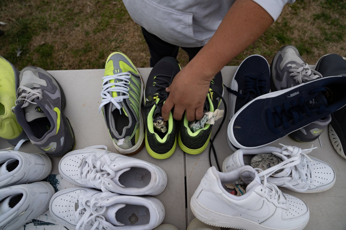 A man’s hand arranges a pair of shoes amid several pairs on a table.
