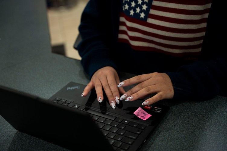 A woman with decorated fingernails and an American flag shirt types on a laptop. Her face is not shown.
