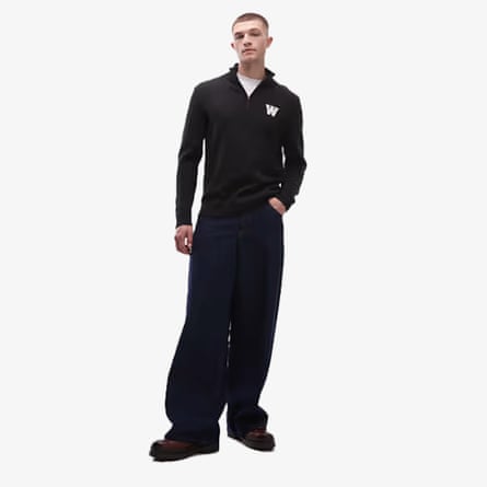 A model wears a Double A By Wood Wood black quarter-zip knitted jumper with large ‘w’ logo on left side of chest. The model also wears large black baggy trousers and a white tshirt.