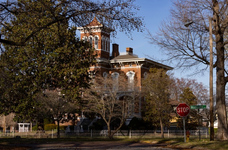 A brick mansion on a tree-lined street.