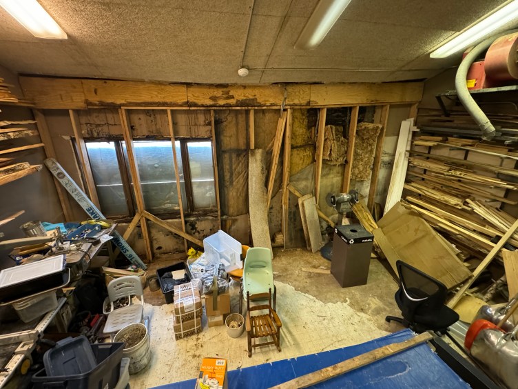 Une pièce pleine de restes de bois. Le mur est partiellement détruit, laissant apparaître une isolation et des poteaux en bois.