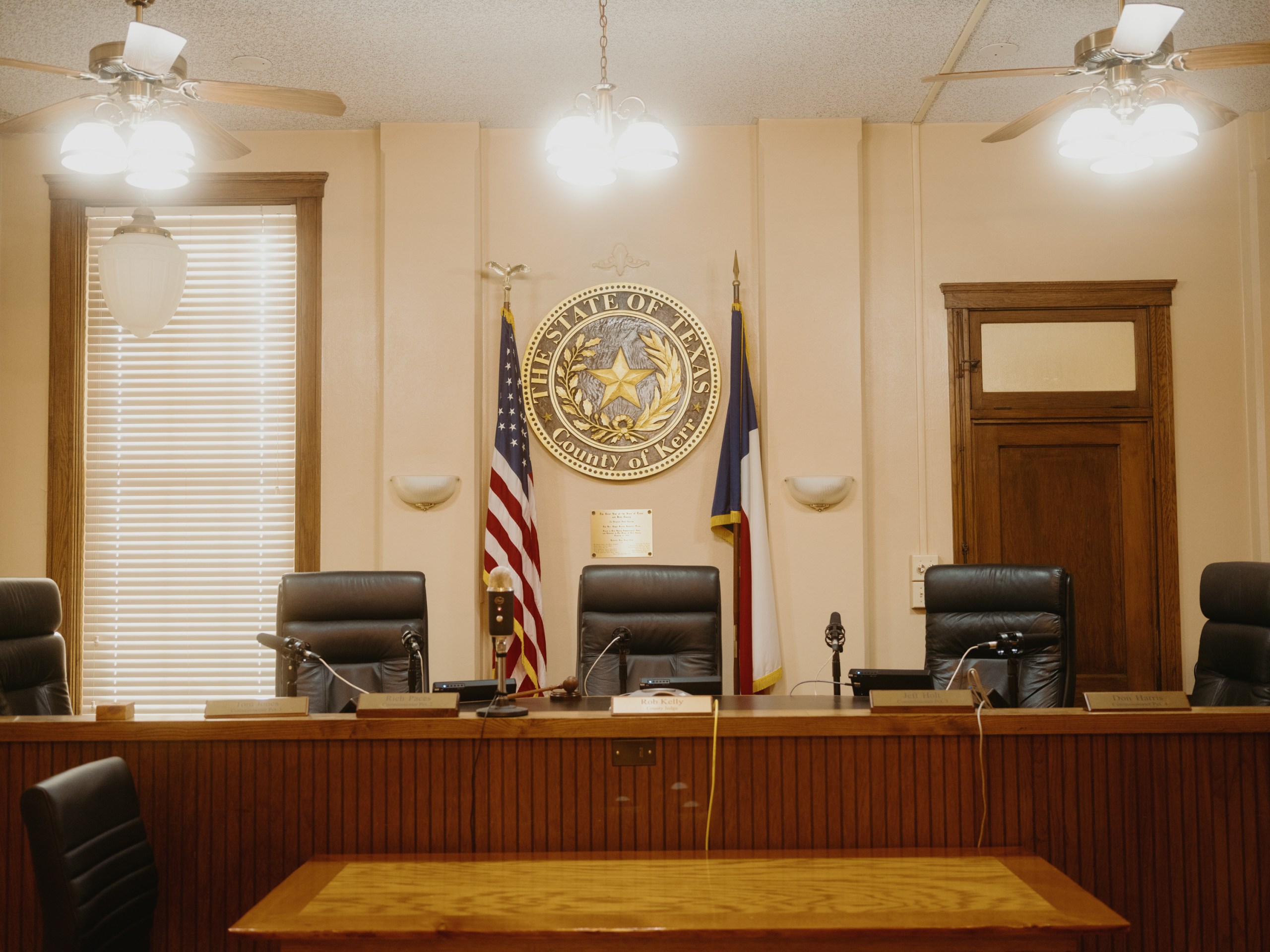 An empty courtroom with five large leather chairs behind the judge’s bench. An American flag and a Texas flag frame a large state seal on the wall.