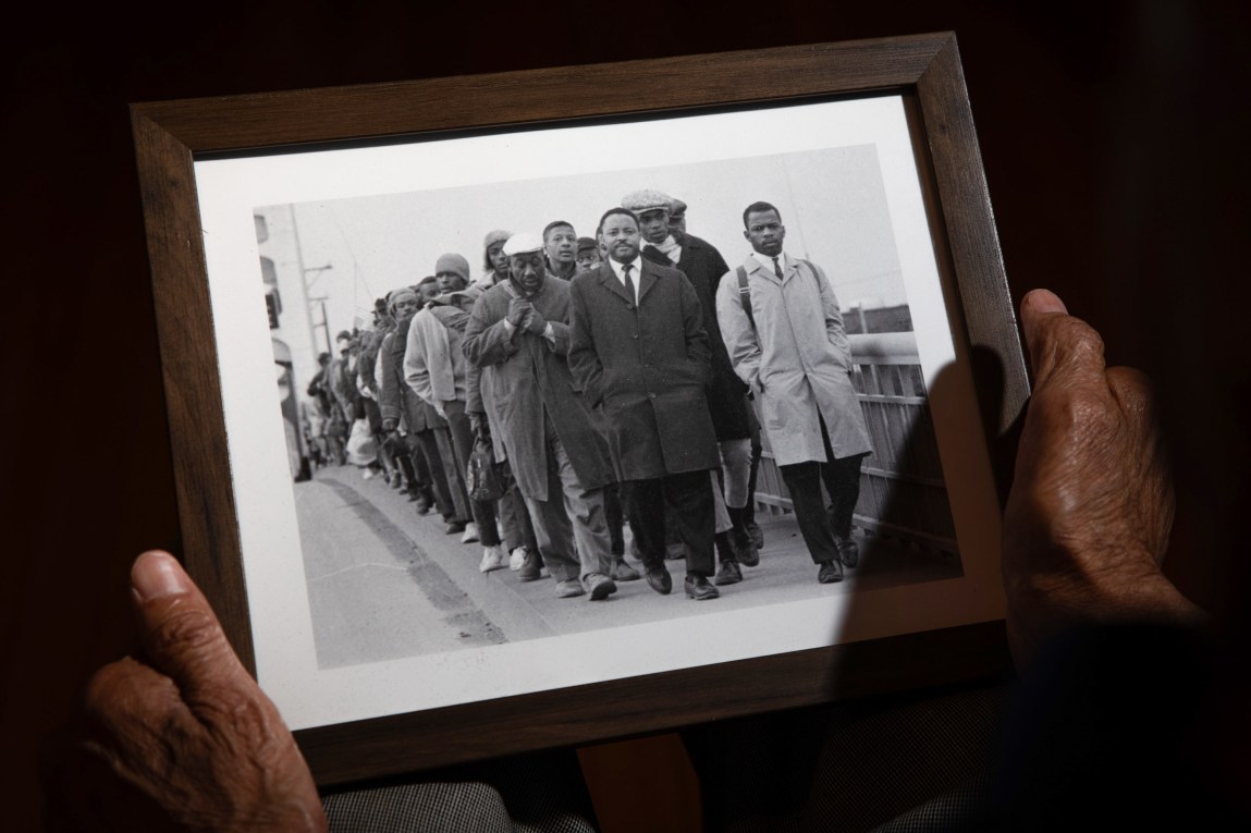 Les mains tiennent une photo encadrée en noir et blanc d’une file de personnes traversant un pont.