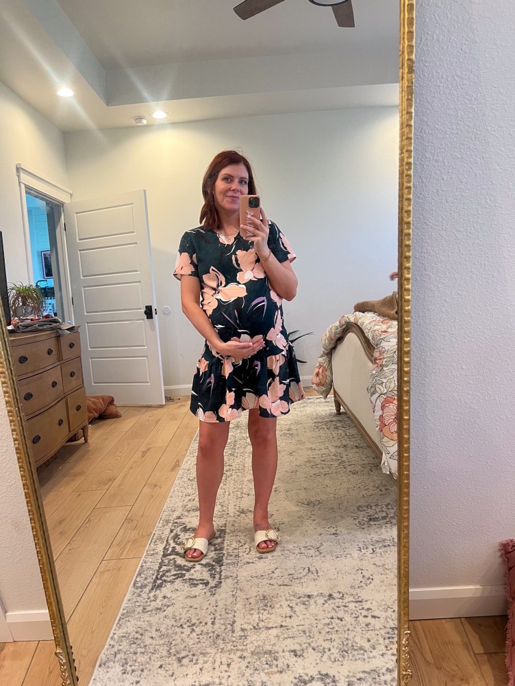 A pregnant woman takes a photo of herself with her phone in the mirror of her bedroom, with one hand holding her belly.