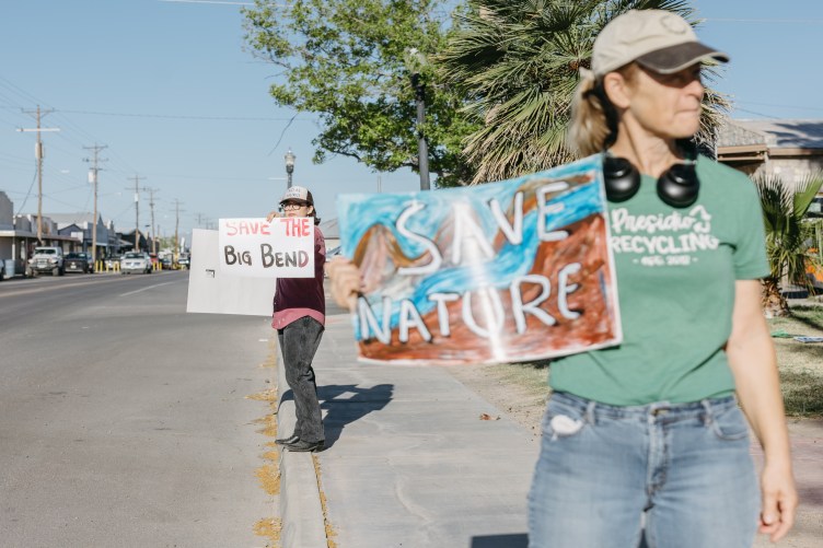 Demonstranten stehen auf einem Bürgersteig entlang einer Straße und halten Schilder mit der Aufschrift „Save the Big Bend“ und „Save Nature“ hoch.