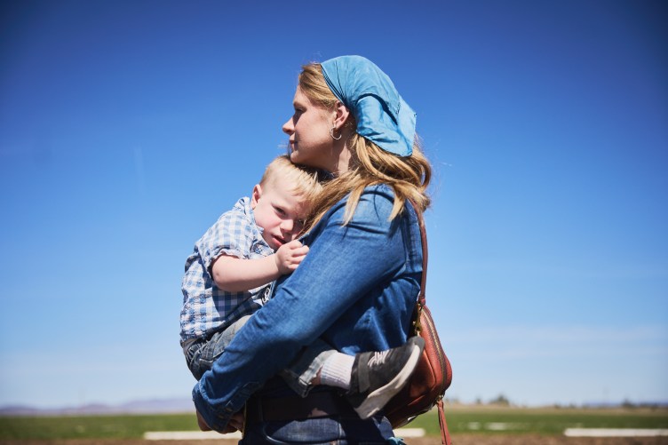 A woman in a denim shirt with a bandana tying her hair back holds a small child.