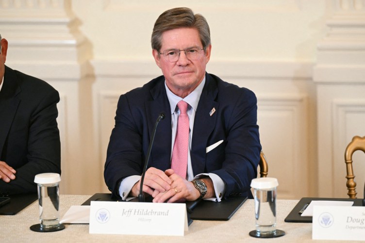 A man in a suit sits at a table with a name tag in front of him.
