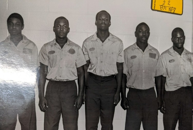 Five young men stand in a lineup photo with serious expressions. They are all wearing the same uniform.
