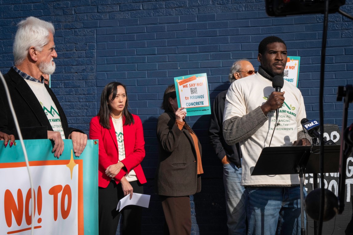 A man speaks into a microphone while several other people stand around and behind him with protest signs.