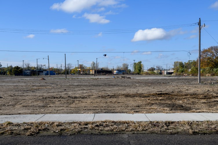 A black bird flies through an empty lot.
