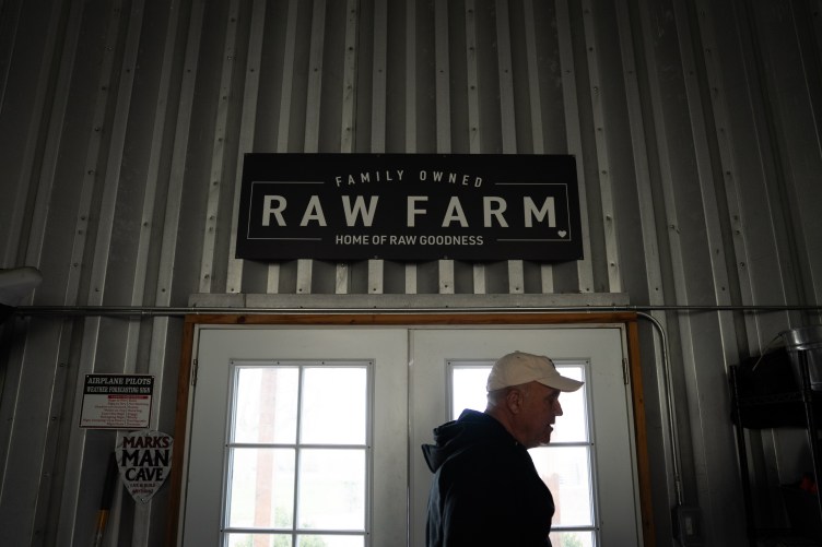 Ein Mann mit Baseballkappe kommt unter einem großen „Raw Farm“-Schild aus einer weißen Doppeltür.