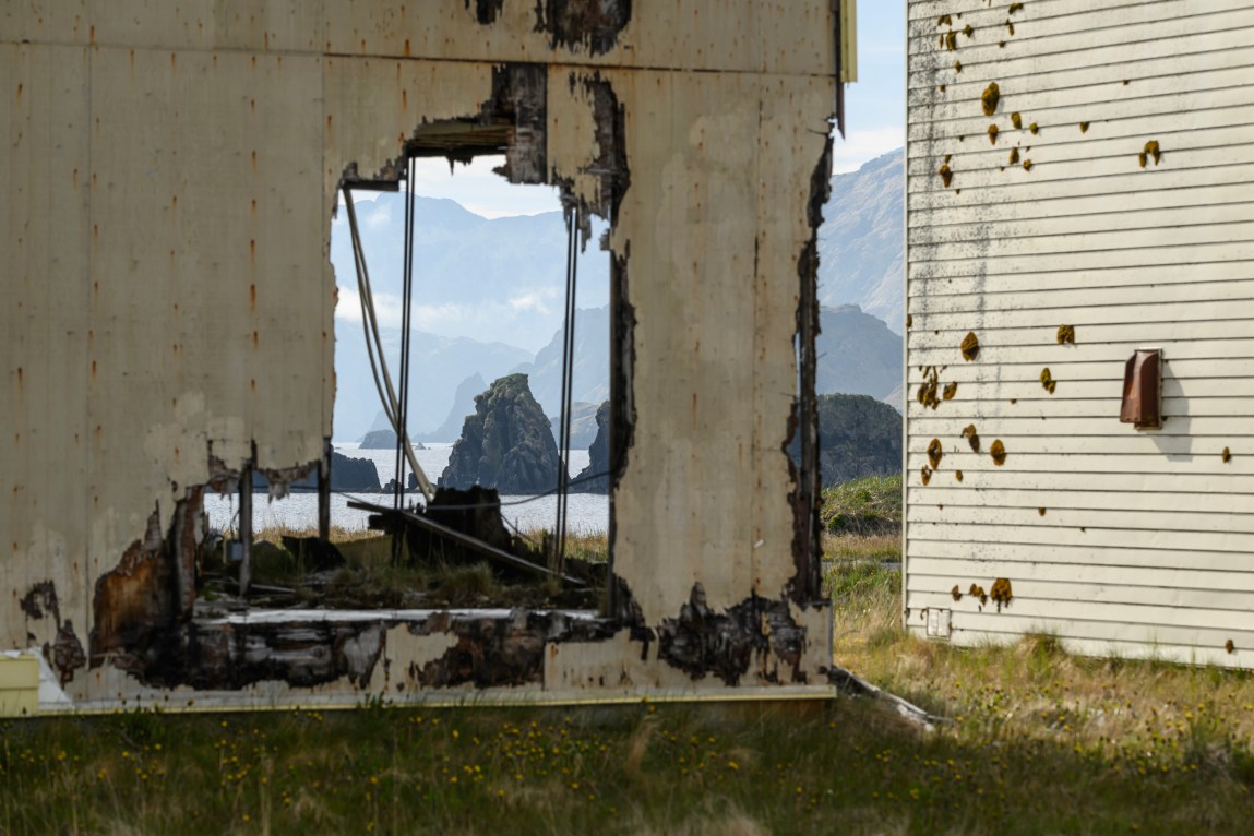 Mountains and water can be seen through the holes of an exterior wall.