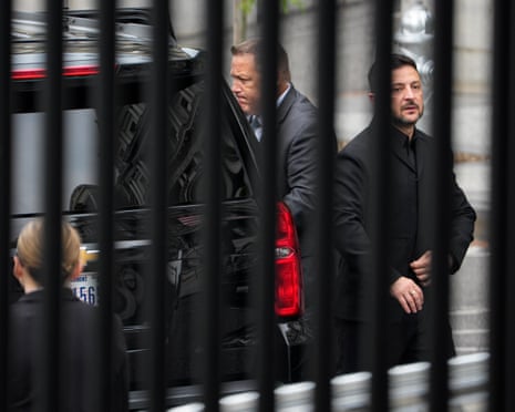 Volodymyr Zelenskyy seen through a tall fence as he gets out of a black car.