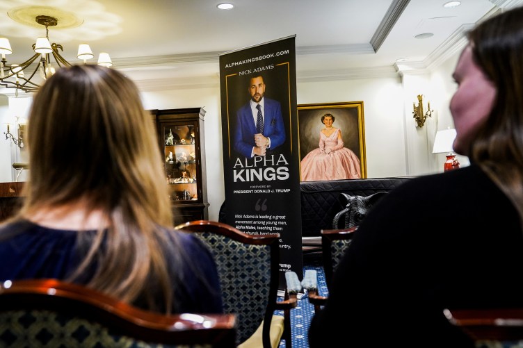 A big banner showing a man in a suit and the words “Alpha Kings” is displayed in an ornate event room. Behind the banner is a large painting of a woman in a pink dress.
