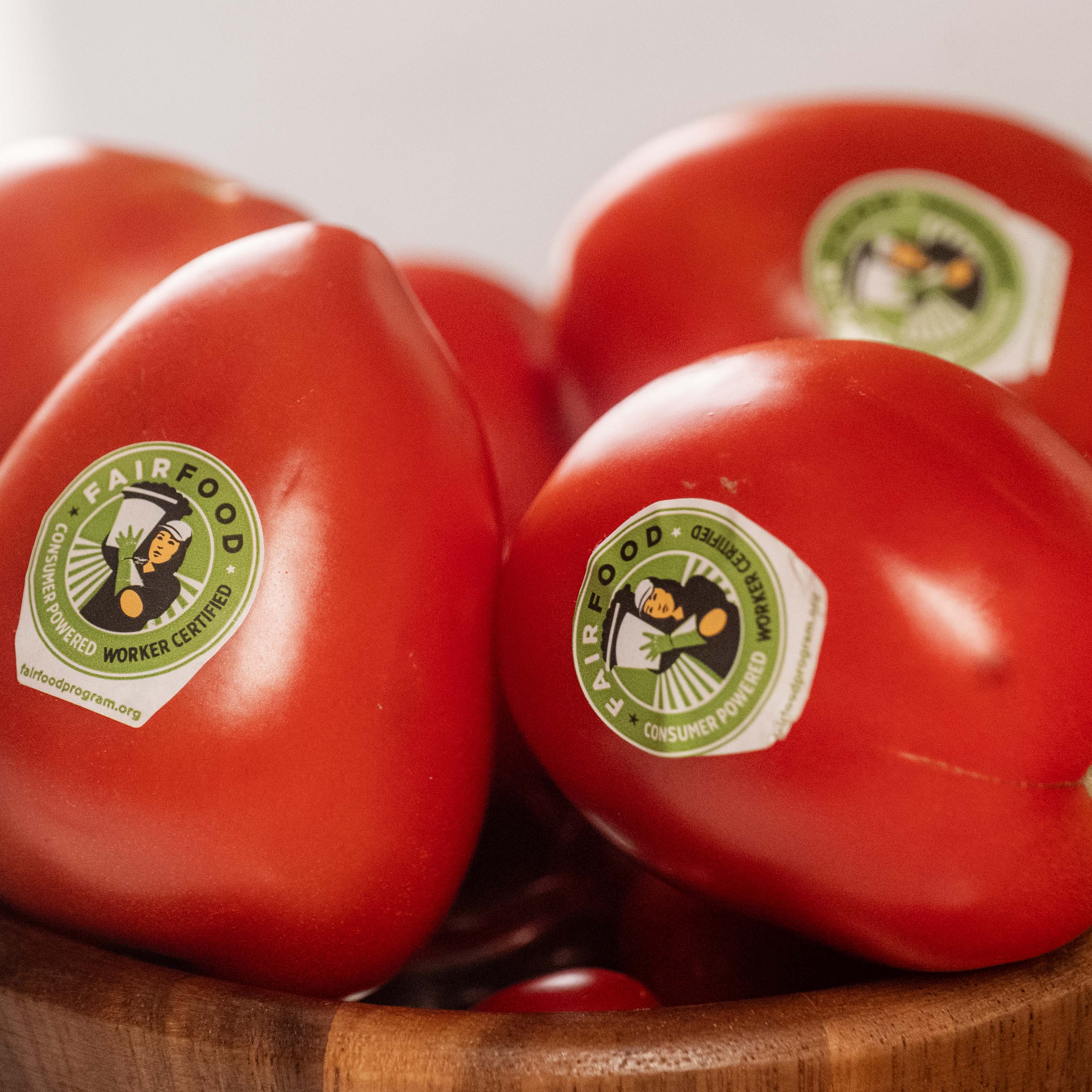 Tomates avec autocollants « Fair Food » dans un bol en bois.