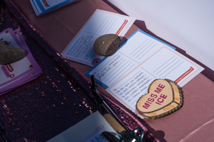 Several postcards with handwritten supportive messages rest on a pink tablecloth, held down by smooth stones.