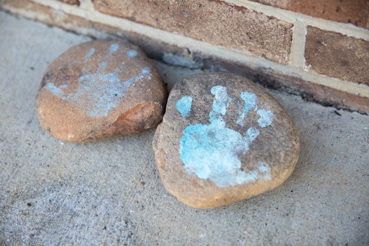 Small light-blue handprints decorate two rocks sitting on cement next to a brick wall.