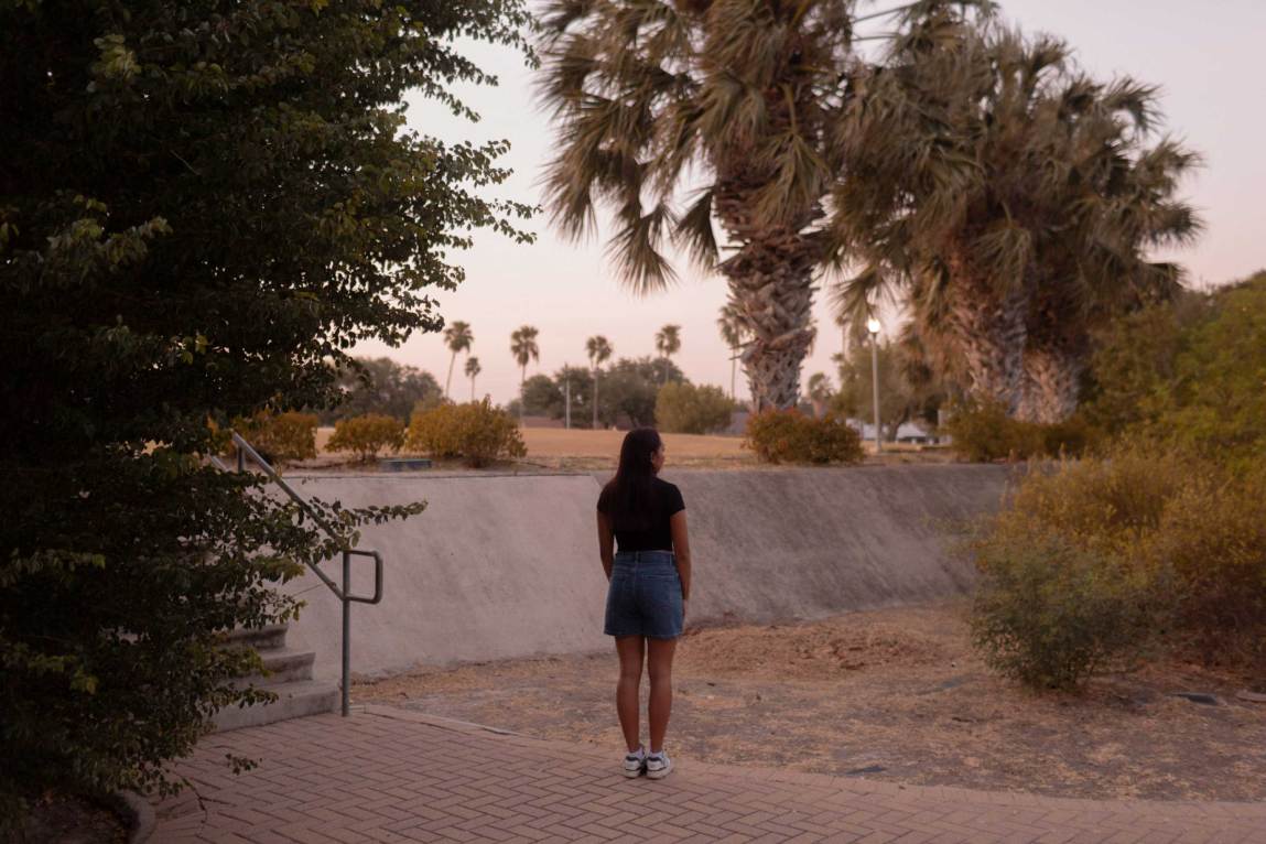 A woman standing with her back to the camera in a public park surrounded by palm trees.