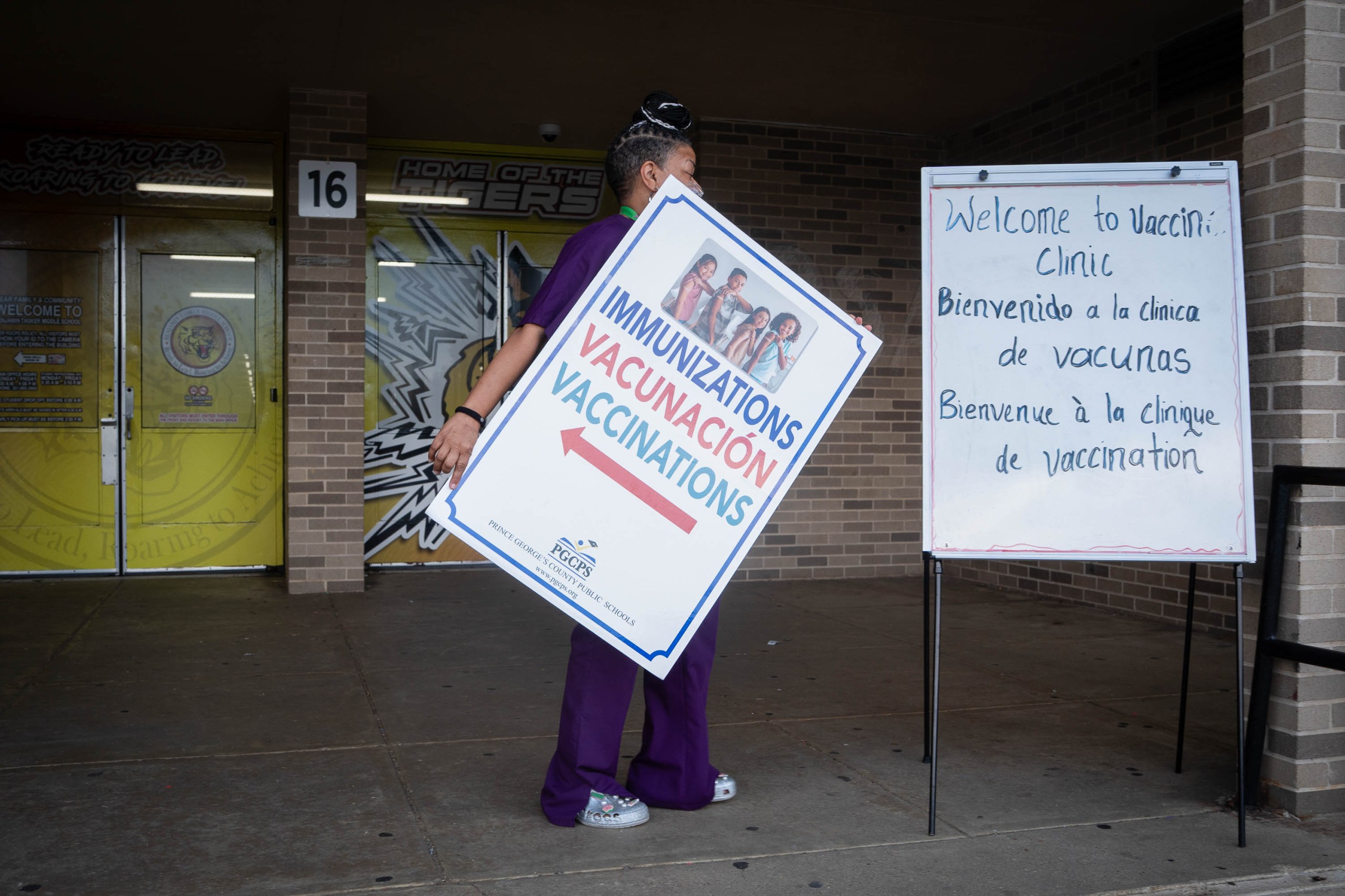 A woman removes a sign, while a second sign announces a vaccine clinic outside a middle school.