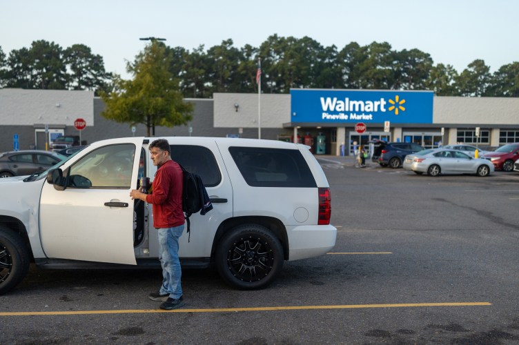 A man with a backpack opens a car door in a Walmart parking lot.