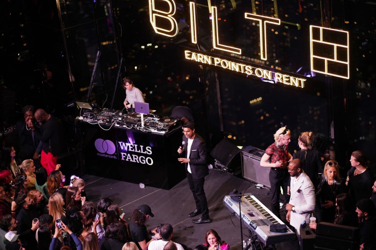 A man in a suit speaks to a crowd from a stage, in front of a sign that reads “Bilt” and “earn points on rent.”