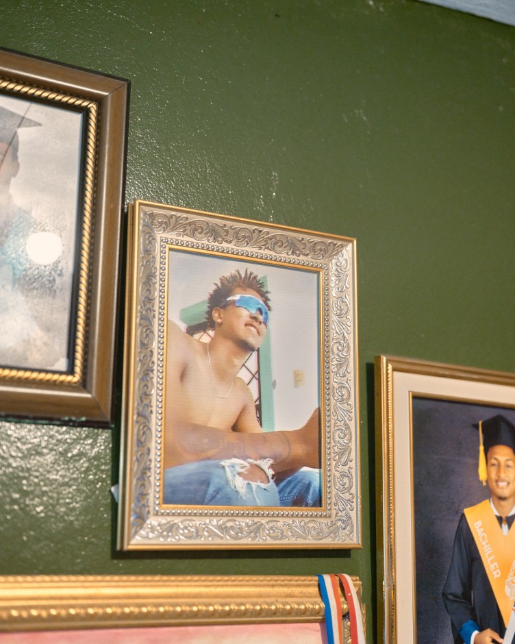 A photo of a man wearing sunglasses and smiling is in an ornate gold frame on a green wall surrounded by other photographs in frames.