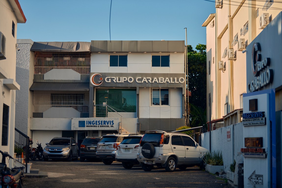 The exterior of the white multistory Grupo Caraballo building with parked SUVs in the front lot.