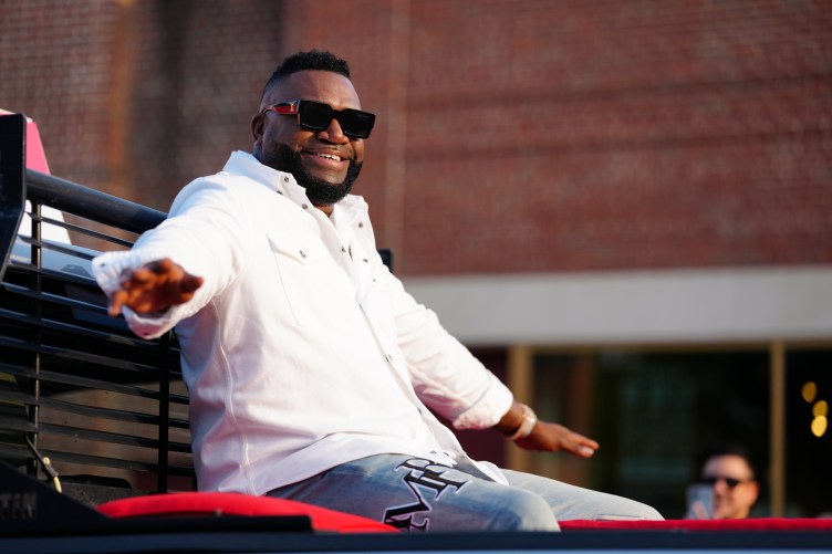 Baseball legend David Ortiz smiles and waves from the back of a vehicle during an outdoor public event.