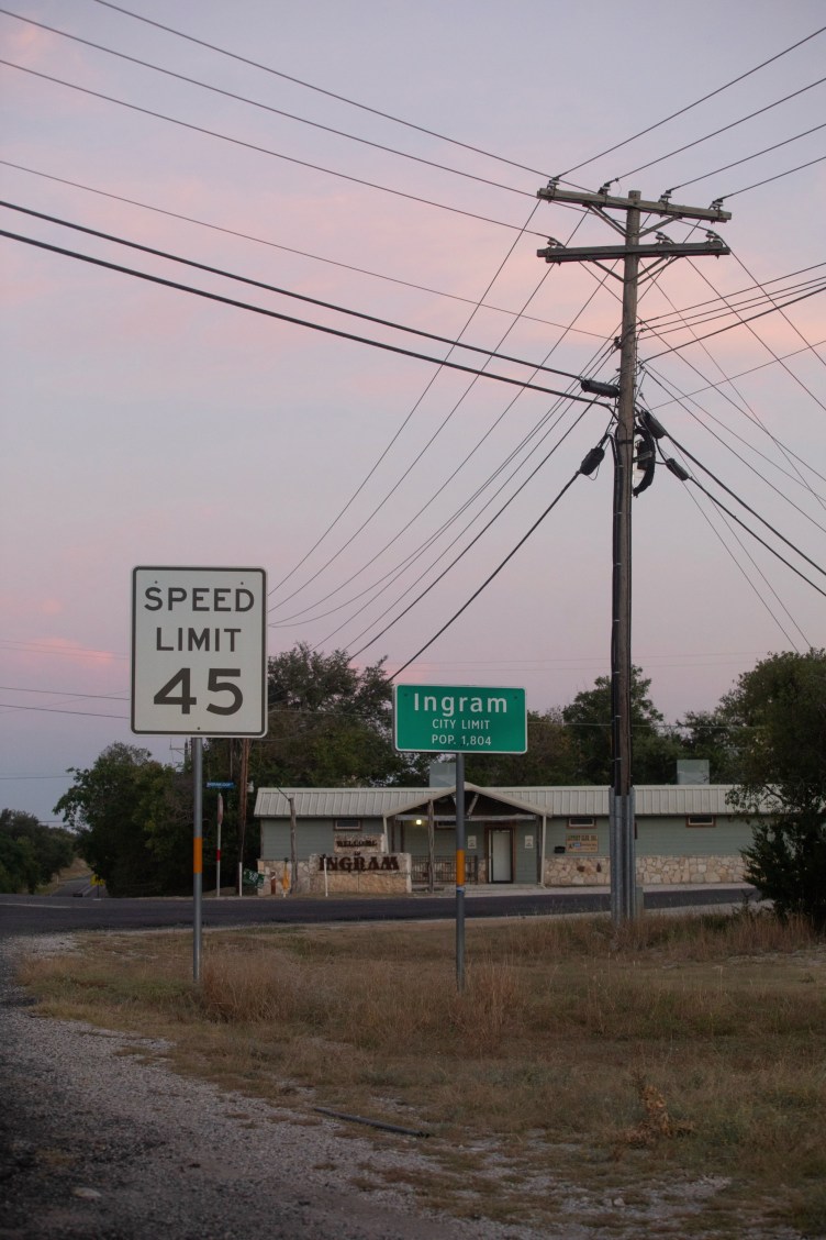 A sign reading “Speed Limit 45” is next to a sign for the city limits of Ingram, which also gives its population as 1,804. In the background, a low-lying building has a sign reading “Welcome to Ingram.”