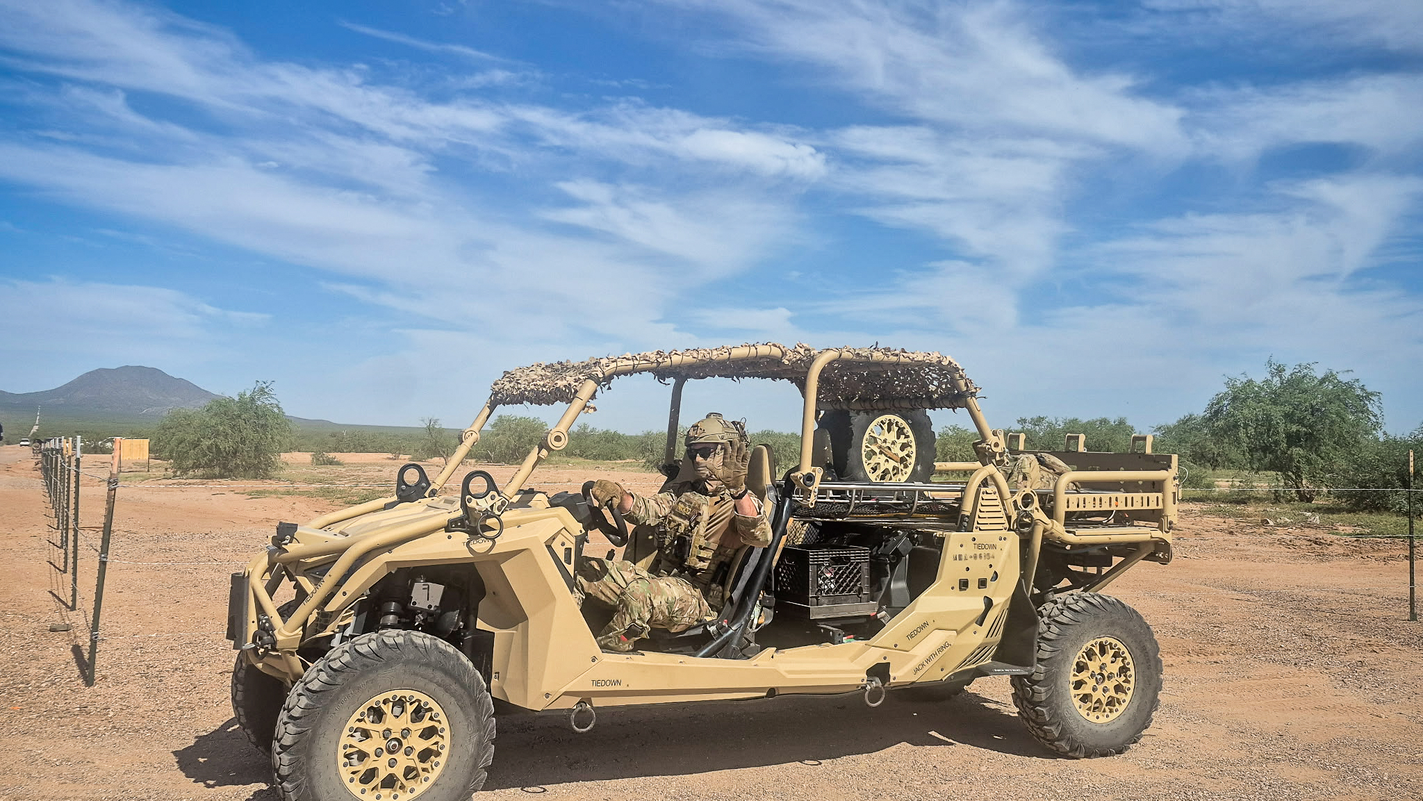 A border patrol agent dressed in tactical gear sits in a tactical vehicle in a desert landscape.
