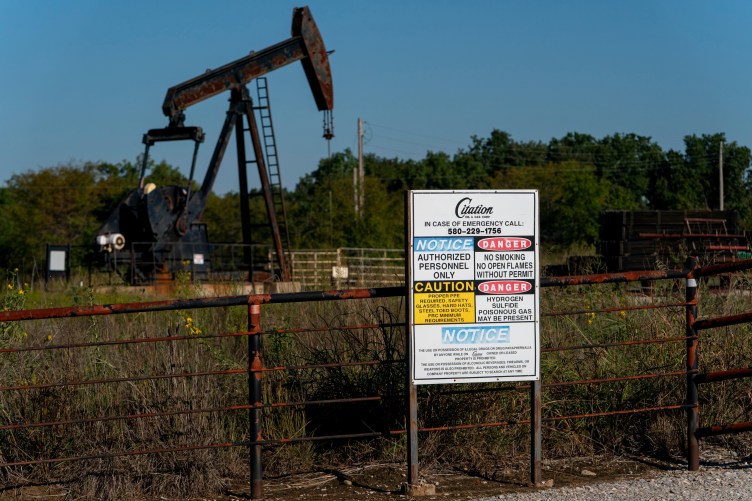 Signage for Citation Oil & Gas on a fence in front of a field with an oil well.