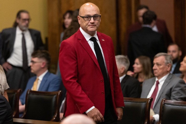 A man wearing a red sports coat walks through a room of people in suits in a government building.