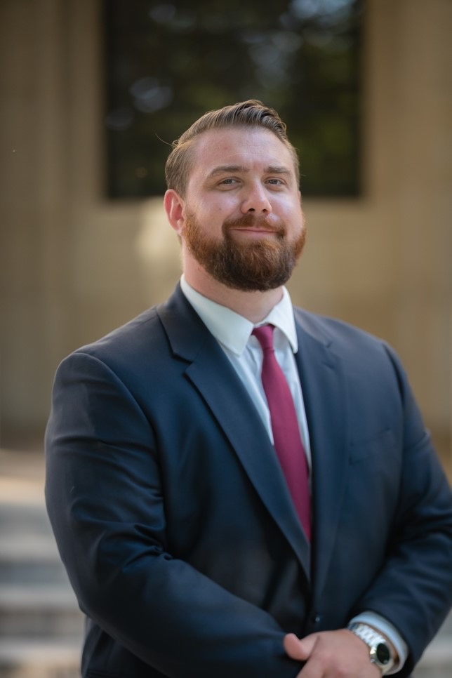 A man with combed-back hair and a beard, wearing a suit and silver watch and slightly smiling at the camera.